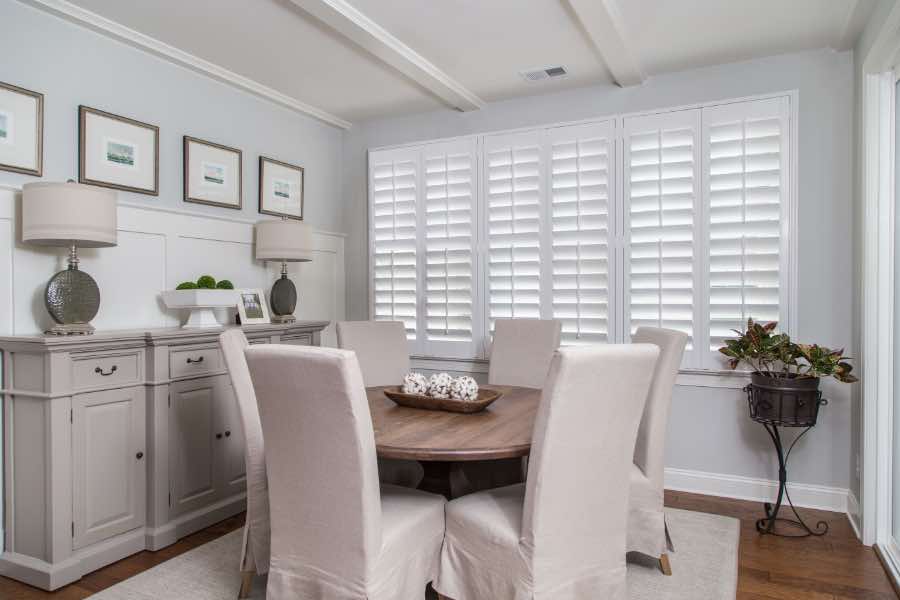 Polywood shutters on a large window in a neutral-colored dining room